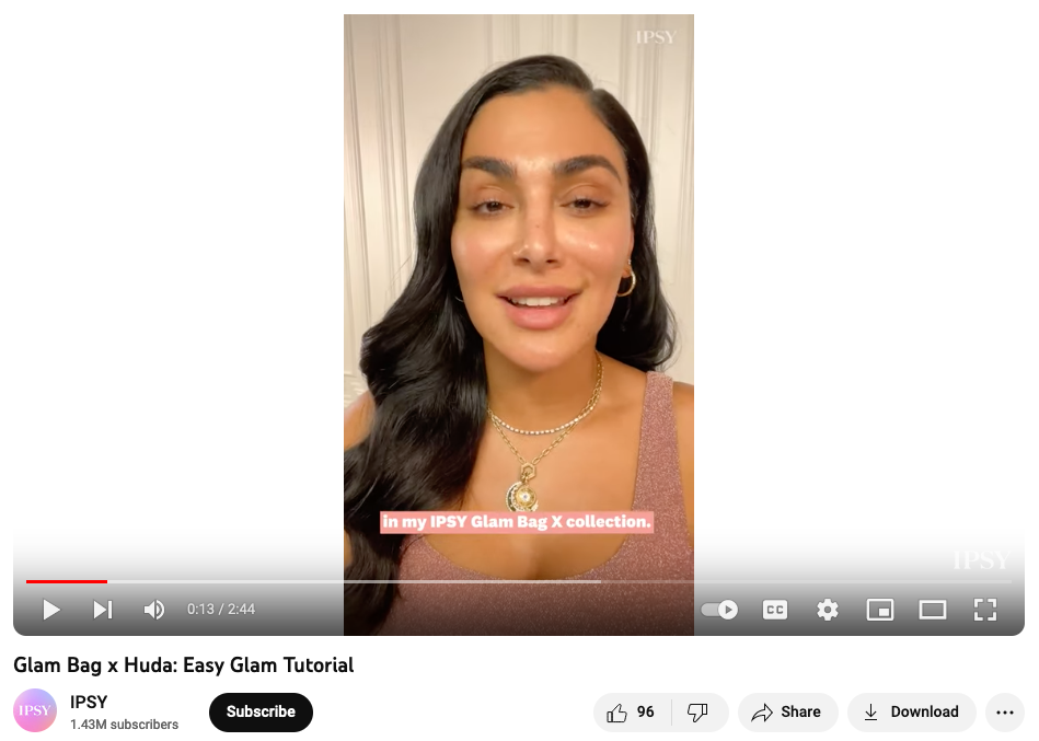 A still from a YouTube video shows beauty influencer Huda Kattan about to begin a makeup tutorial with makeup elements from her Glam Bag created by IPSY as part of the beauty brand's influencer partnership strategy.