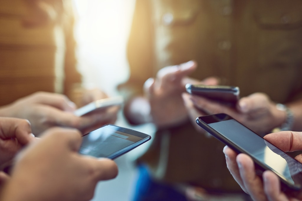 Cropped shot of a group of colleagues using their smart phones in synchronicity. Social media marketing concept